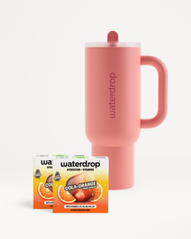 Cană termo Waterdrop roz cu capac și pai, așezată lângă două cutii cu aroma Cola Orange, pe fundal alb.