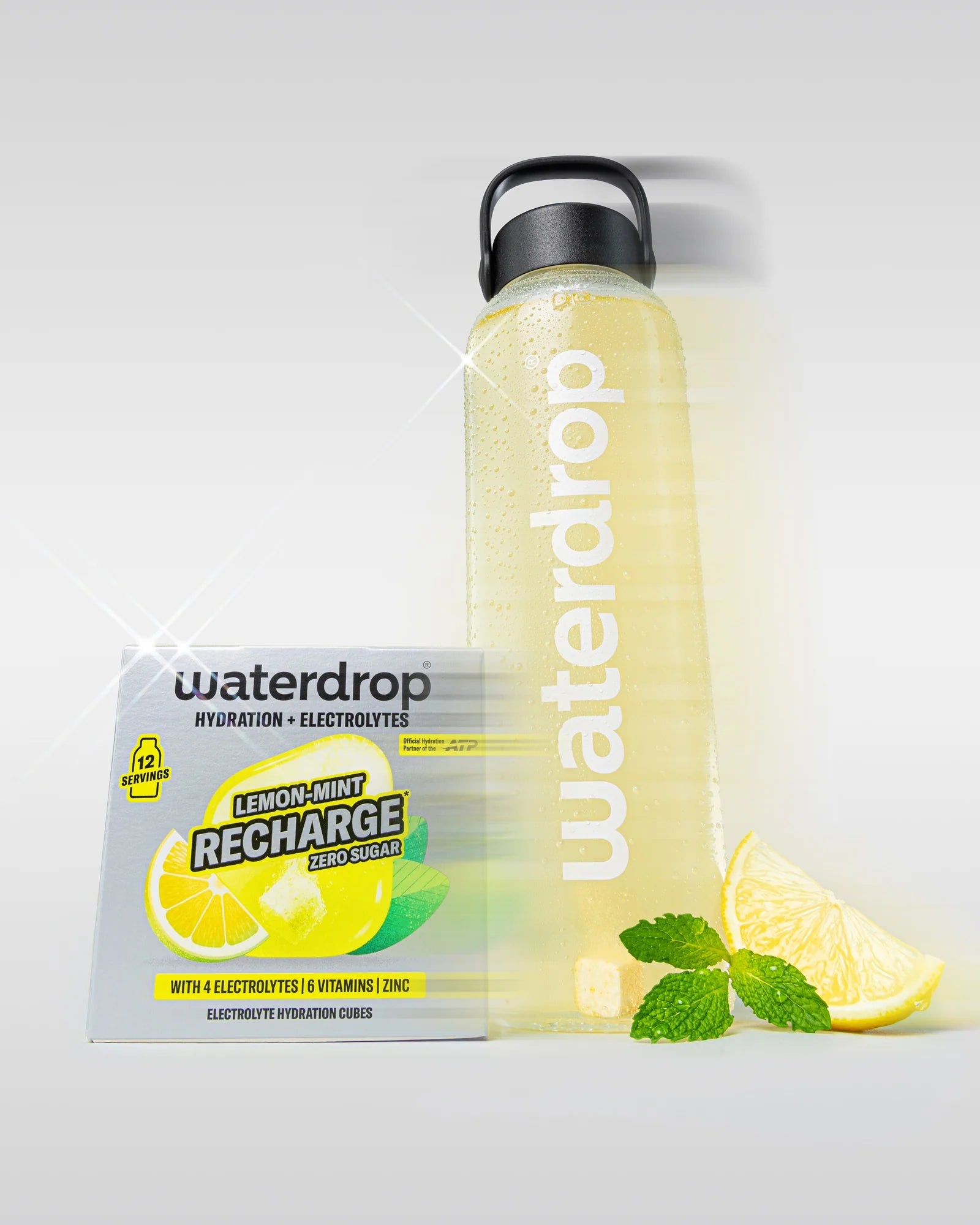 Sticlă reutilizabilă waterdrop umplută cu băutură galbenă, lângă o cutie Lemon-Mint Recharge cu 12 porții, o felie de lămâie și frunze de mentă, pe fundal deschis.