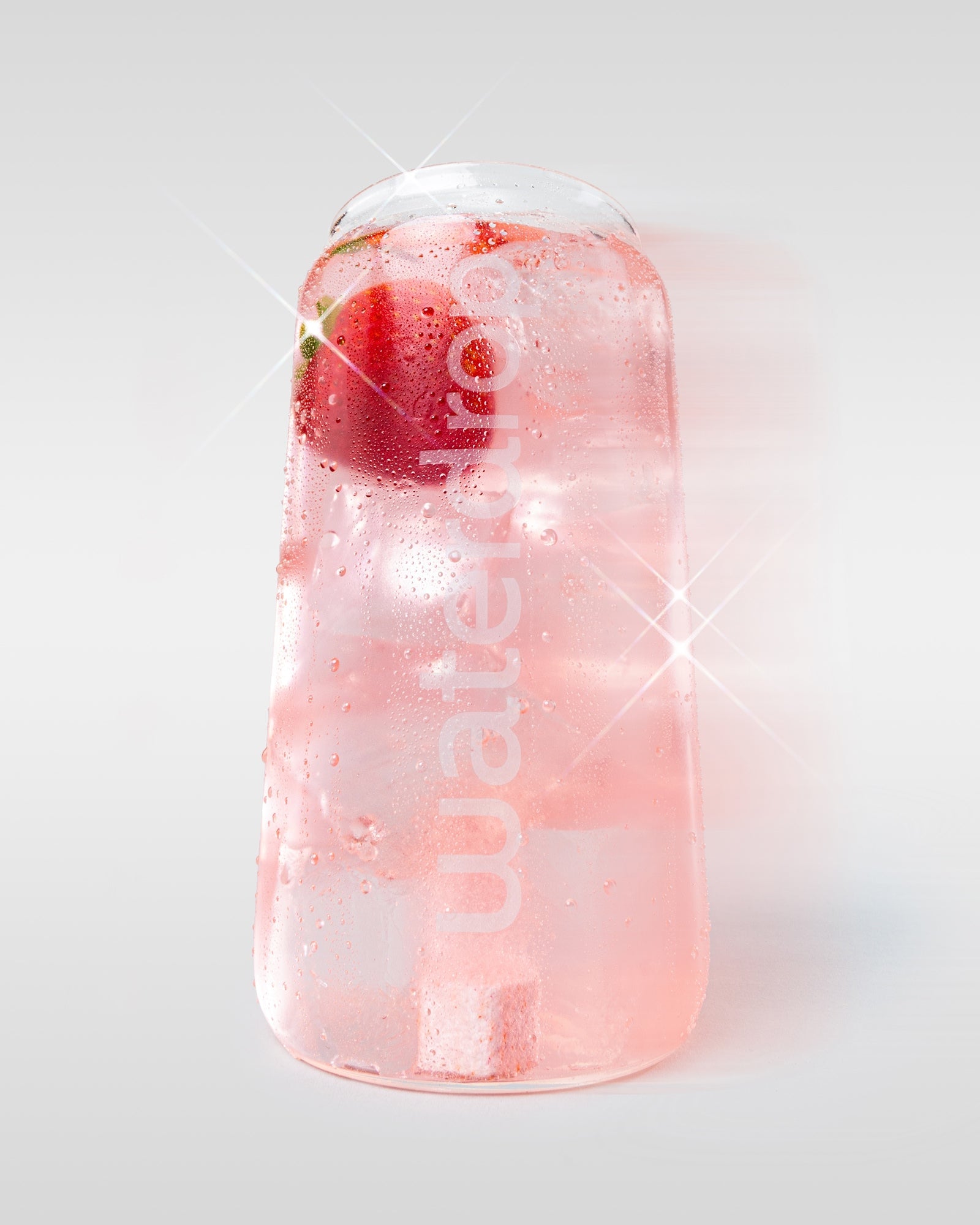 Pahar waterdrop umplut cu băutură roz, cu cuburi de gheață, fruct roșu și un cub de hidratare vizibil, pe fundal deschis.