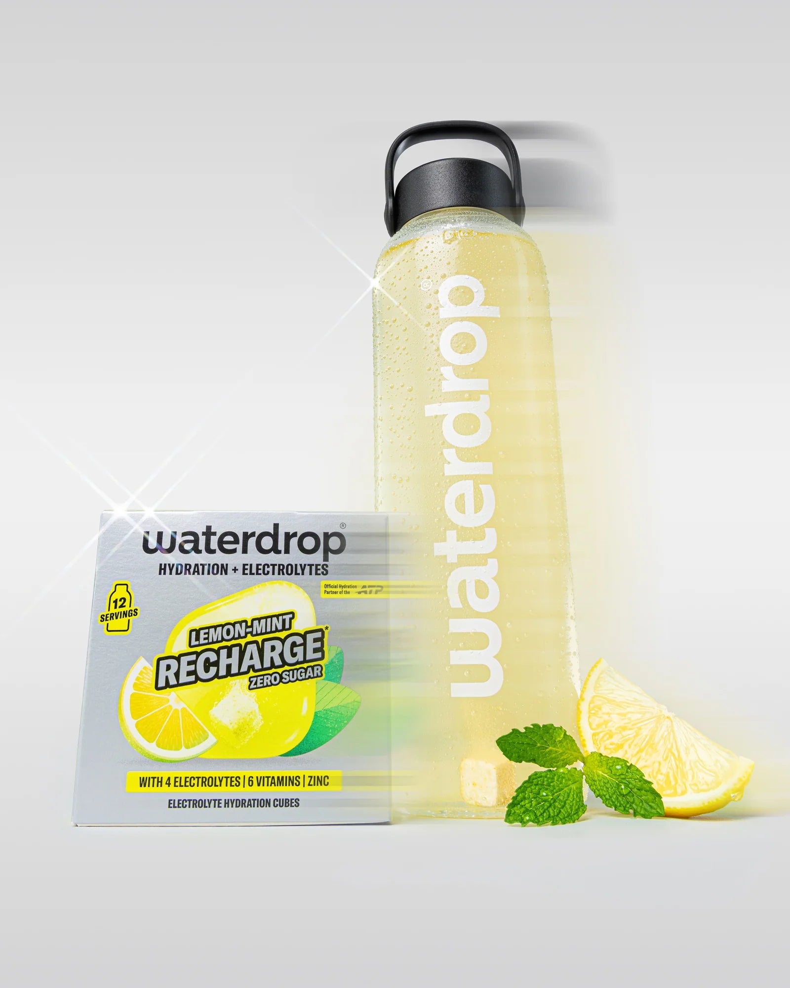 Sticlă reutilizabilă waterdrop umplută cu băutură galbenă Lemon-Mint, lângă o cutie Lemon-Mint Recharge fără zahăr cu 12 porții, felii de lămâie și frunze de mentă, pe fundal alb.