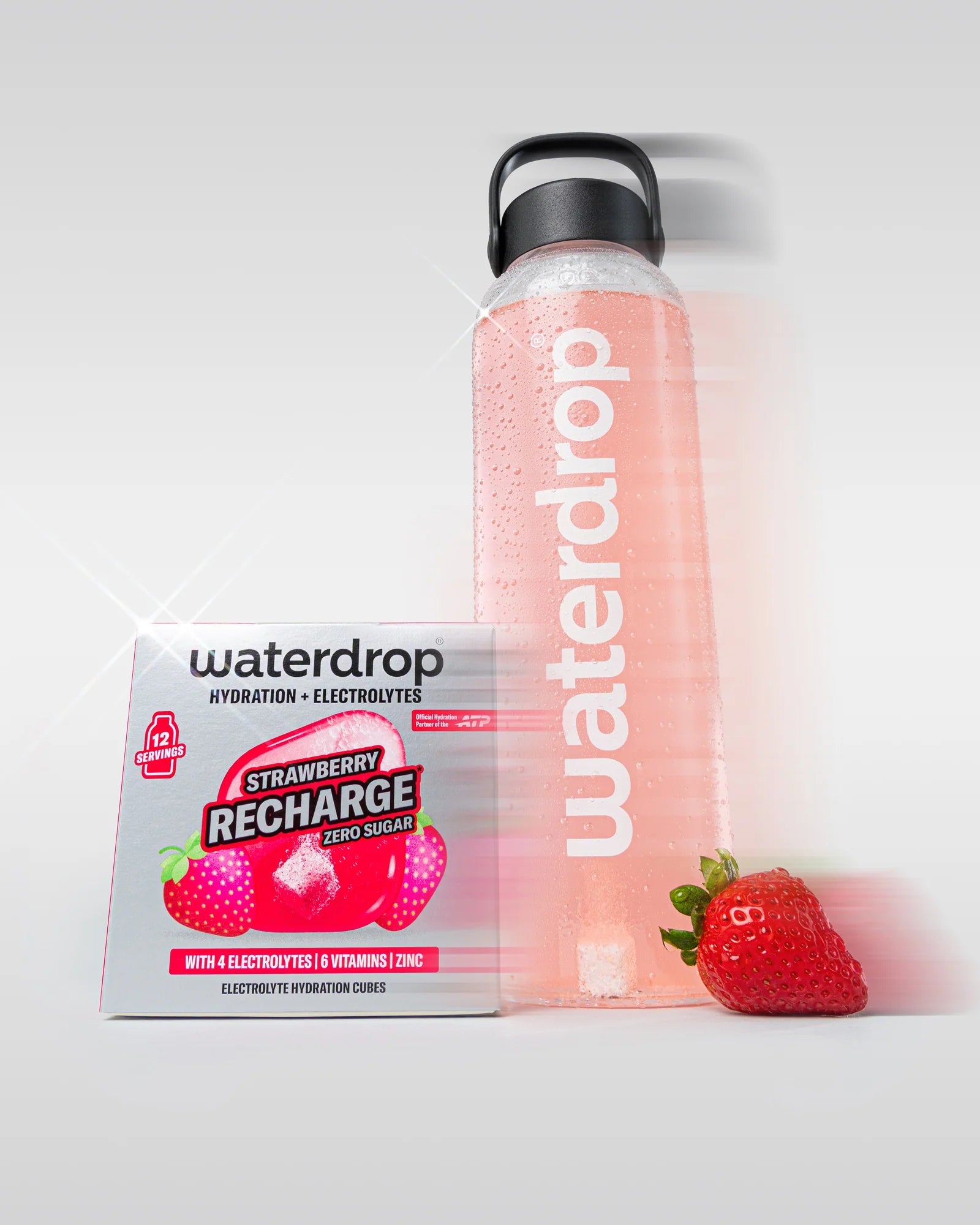 Sticlă reutilizabilă waterdrop umplută cu băutură roz, lângă o cutie Strawberry Recharge fără zahăr cu 12 porții și o căpșună proaspătă, pe fundal alb.