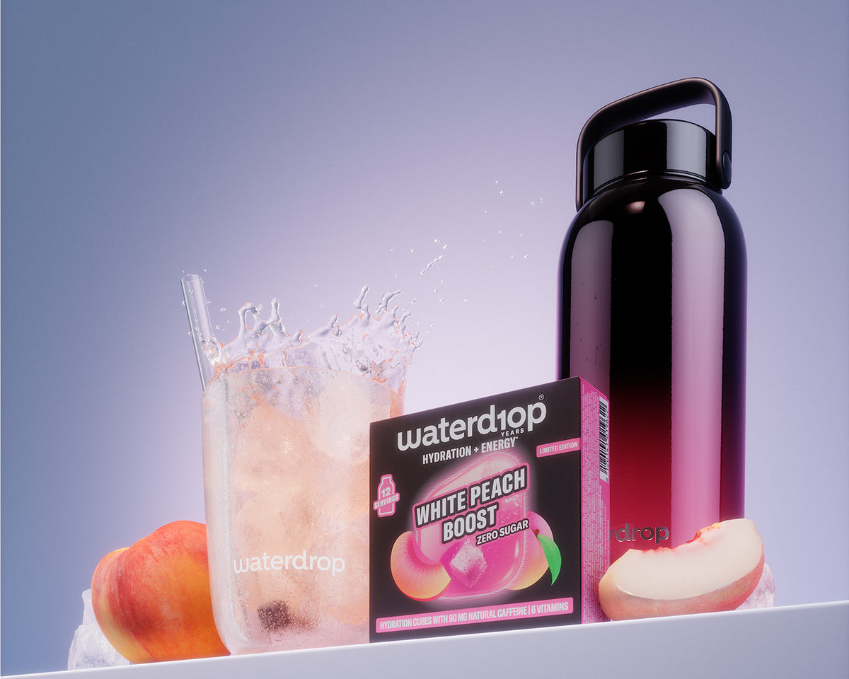 Cutie produs White Peach Boost lângă un pahar cu băutură răcoritoare cu gheaţă şi o sticlă neagră reutilizabilă pe un raft alb.