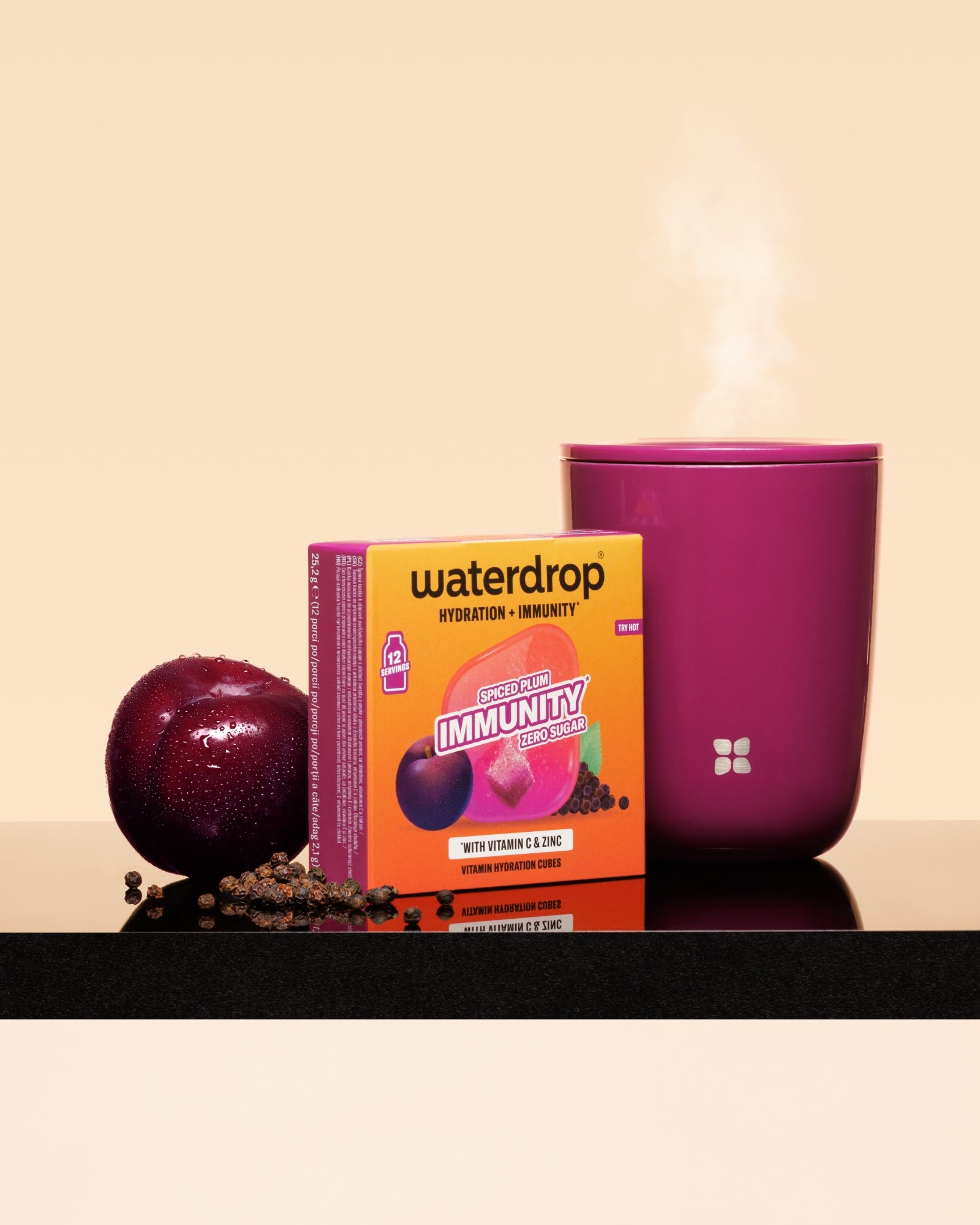 Cutie Waterdrop imunitate cu o prune și o cană roz aburindă pe o suprafață neagră.